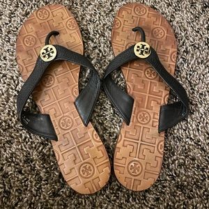 Tory Burch black leather sandal with gold emblem.